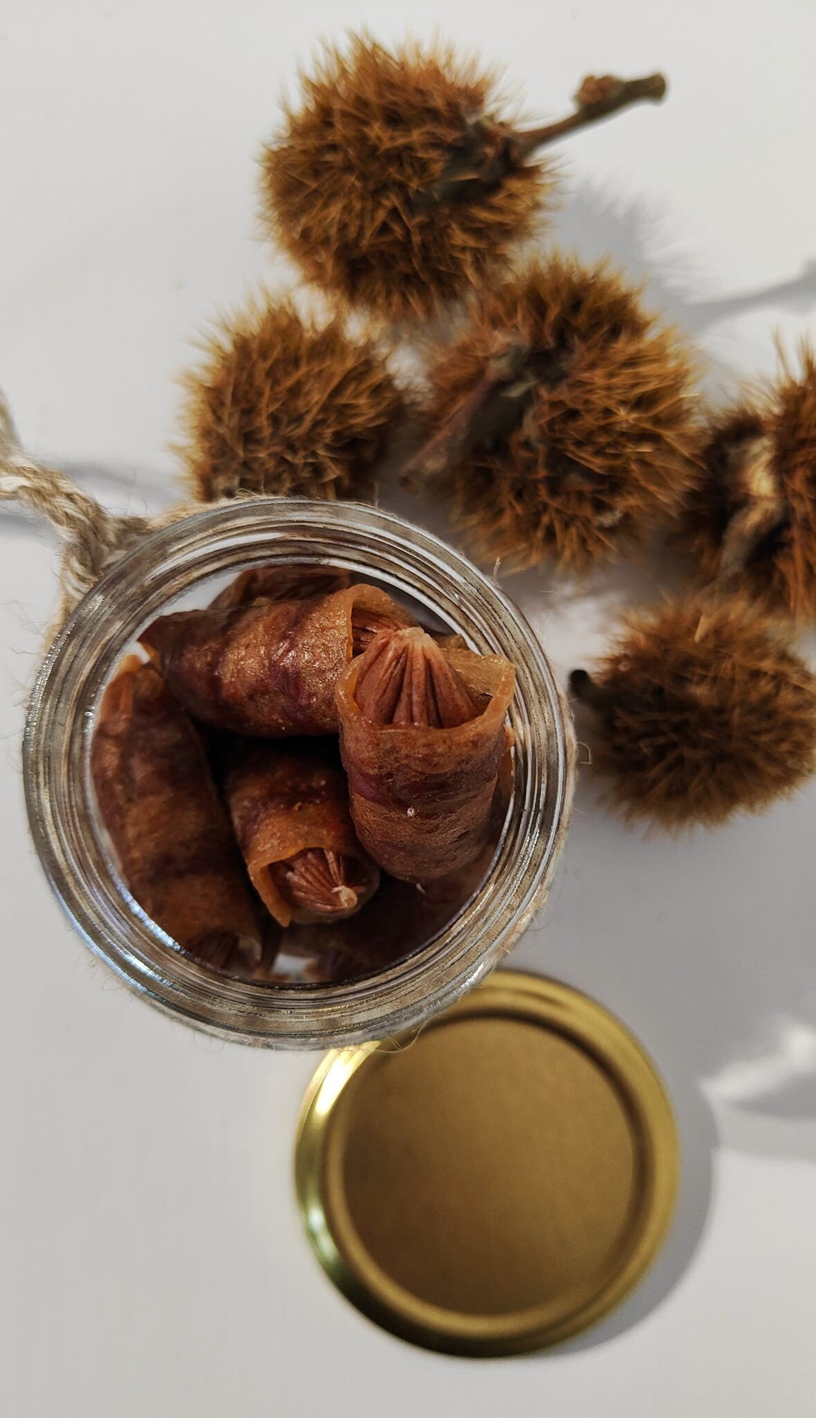 Glass jar with treats inside, gold lid sitting beside and chestnut husks in the background