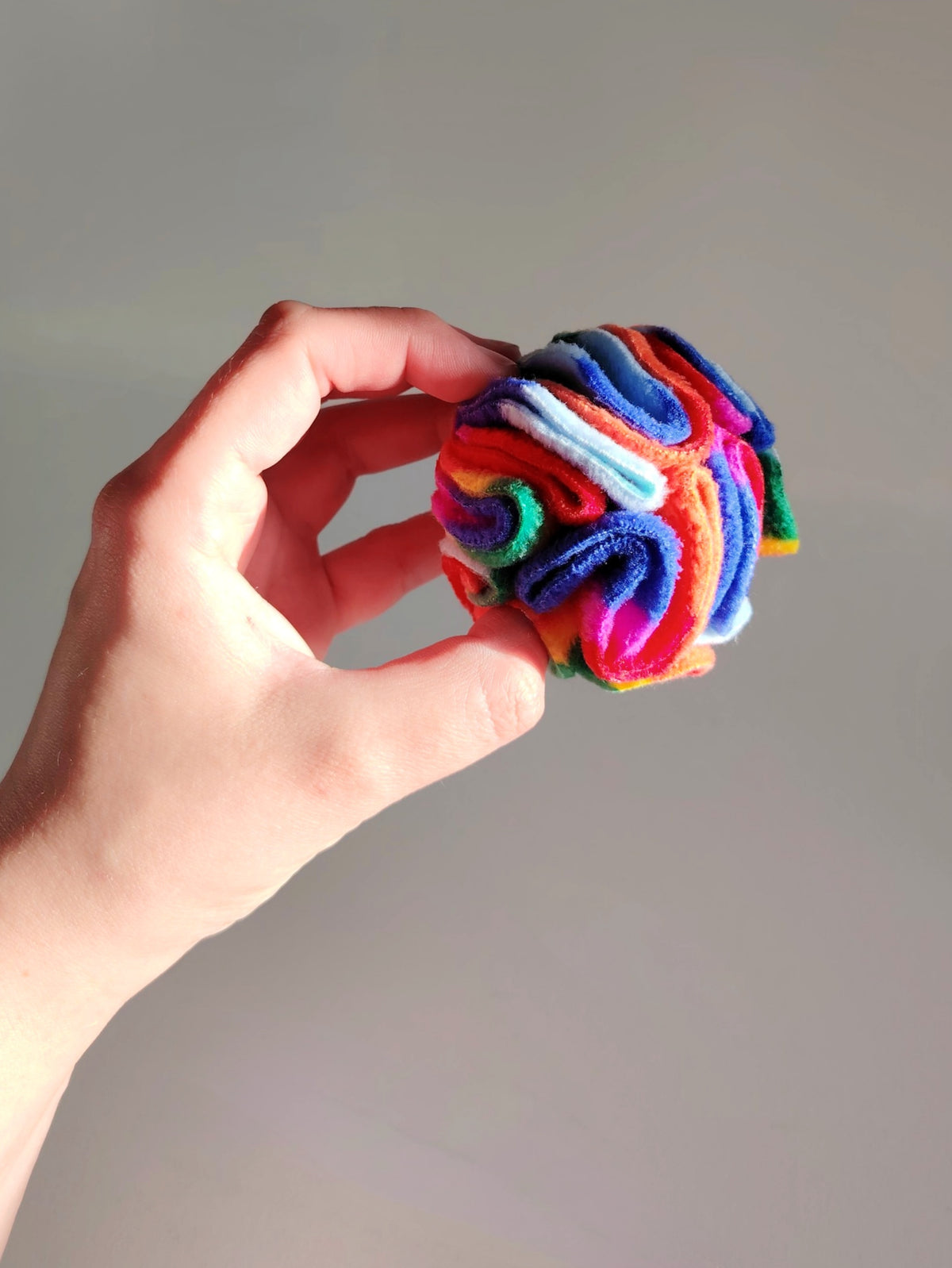 Hand holding a Rainbow Pocket Snuffle Ball dog enrichment toy to show small size