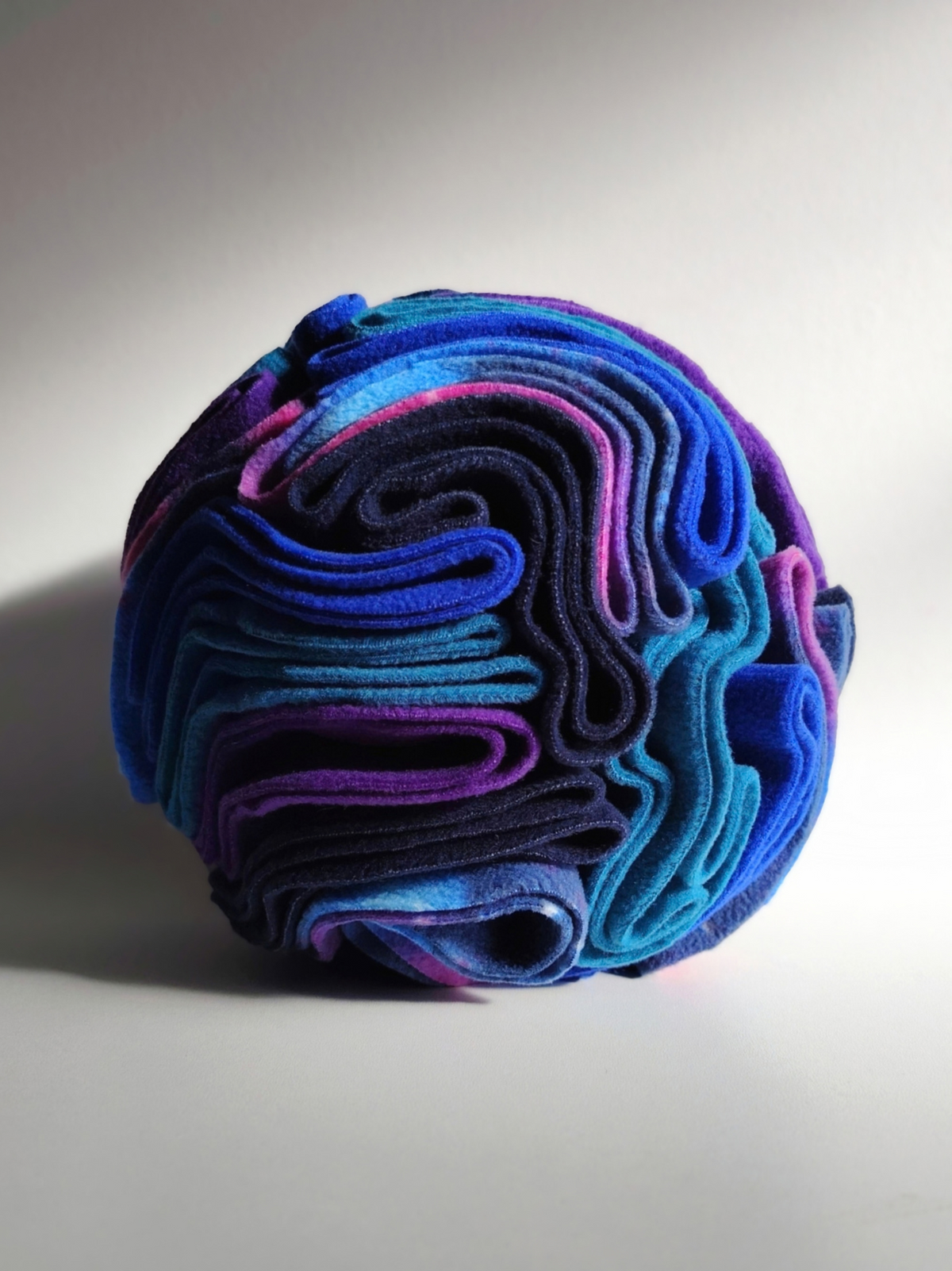 Close-up of a Nova Zeal Night Sky Pocket Snuffle Ball, showing tightly folded navy, royal blue, teal, purple and galaxy-patterned fleece designed for hiding treats and encouraging foraging.