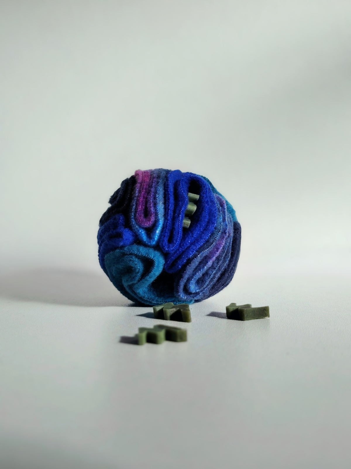 Nova Zeal Night Sky Pocket Snuffle Ball in navy, royal blue, teal and purple fleece, displayed with small green dog treats on a white background.