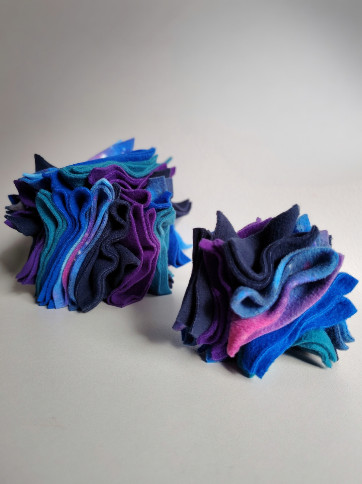 Large and small Nova Zeal Night Sky Scruffle Balls displayed side by side on a light background, showing their different sizes and layered navy, royal blue, teal, purple and galaxy-patterned fleece.