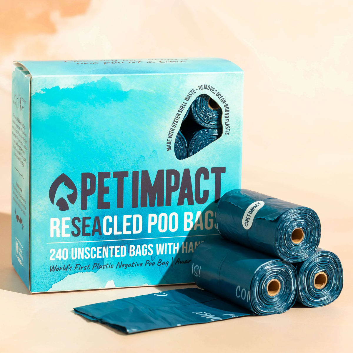 Box of Pet Impact ReSEAcled dog poo bags displayed with several blue rolls and one unfolded bag on a pale background.