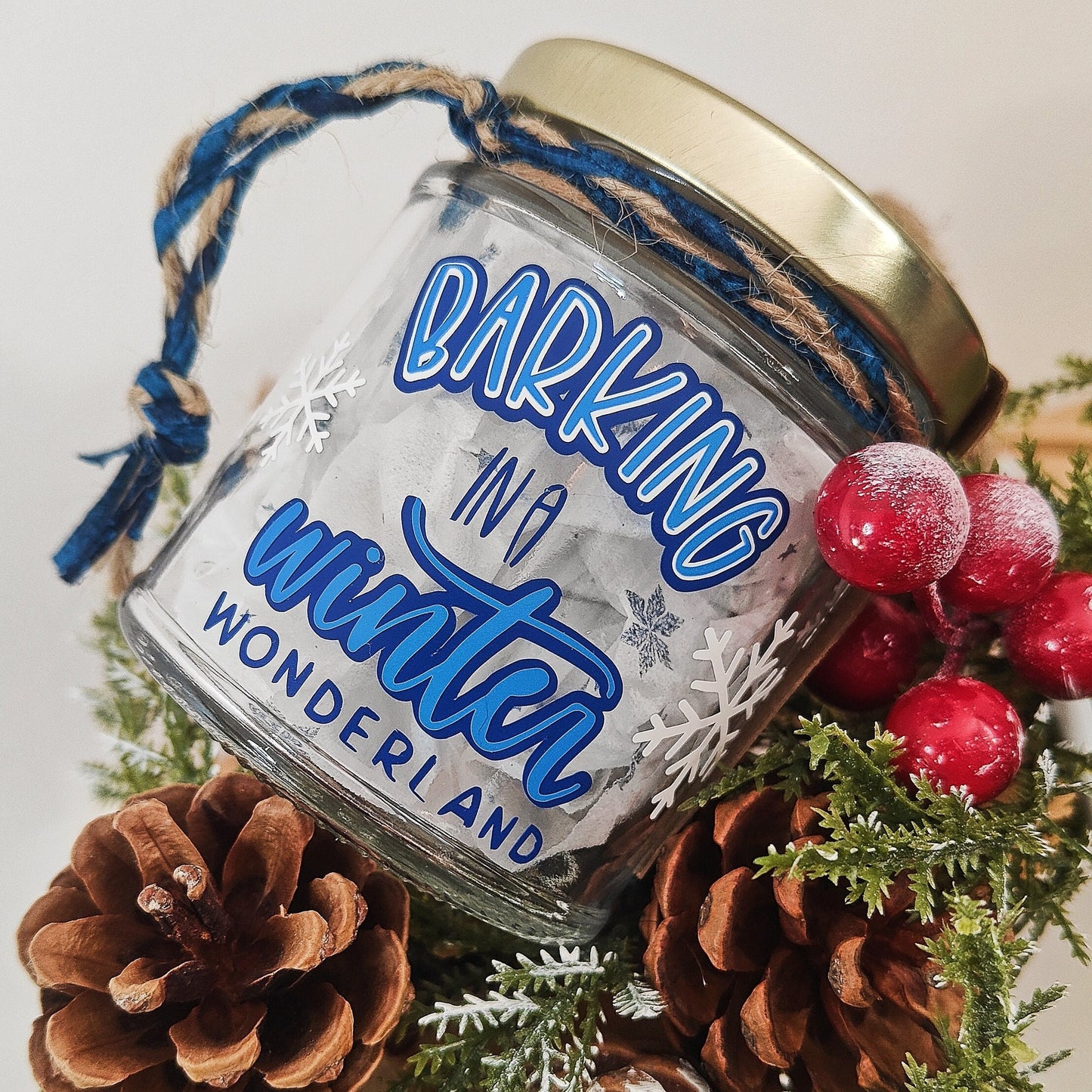 Decorative glass jar with 'Barking in a Winter Wonderland' text, surrounded by pinecones and berries.
