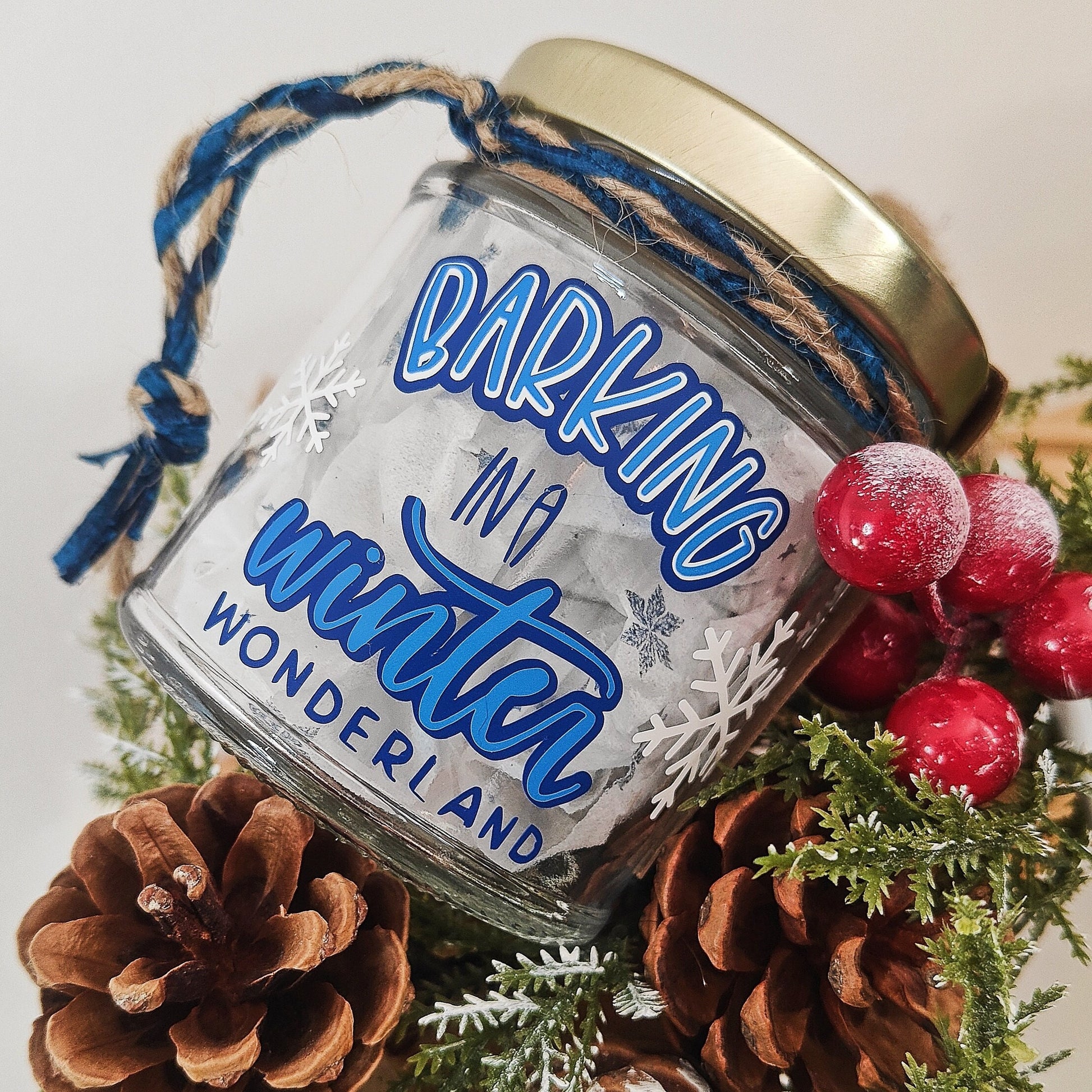 Decorative glass jar with 'Barking in a Winter Wonderland' text, surrounded by pinecones and berries.