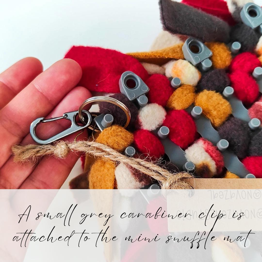 Colourful mini snuffle mat with a small grey carabiner clip attached, held by a hand.