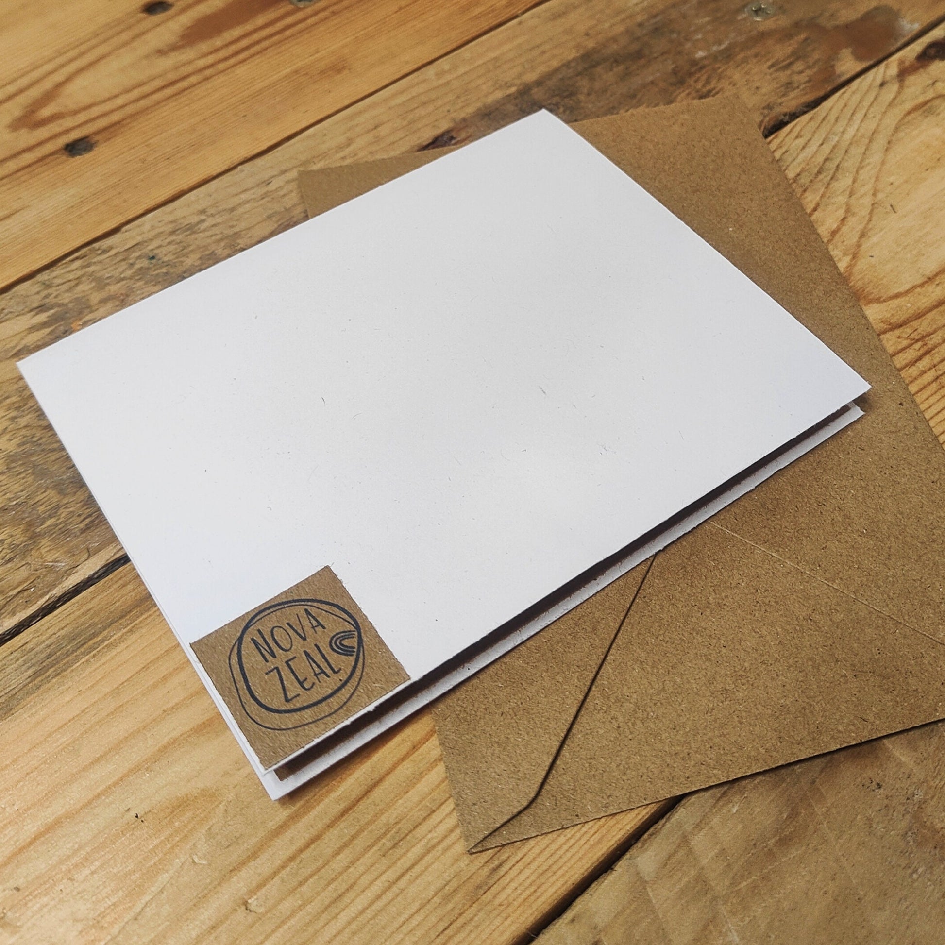 White card with brown envelope on a wooden surface, featuring 'Nova Zeal' branding on the reverse of the card.