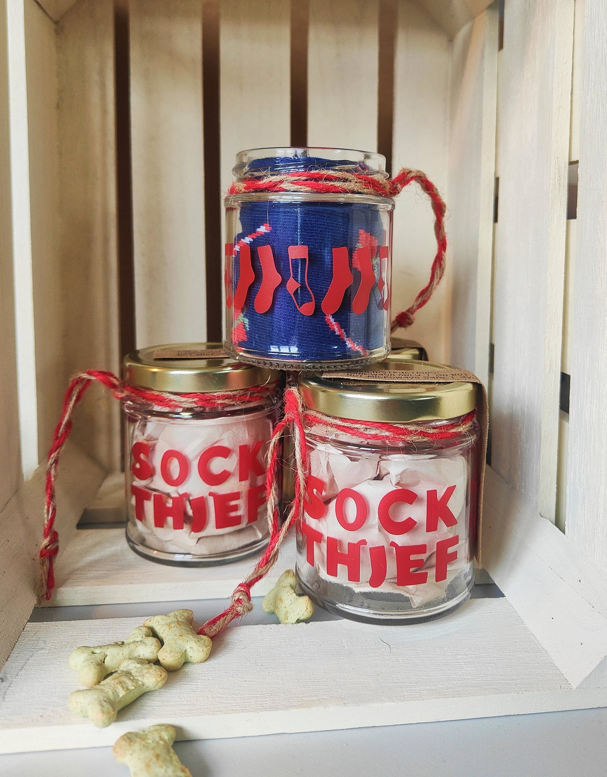 Three glass jars with decorative labels on a wooden shelf. Scattered treats surrounding