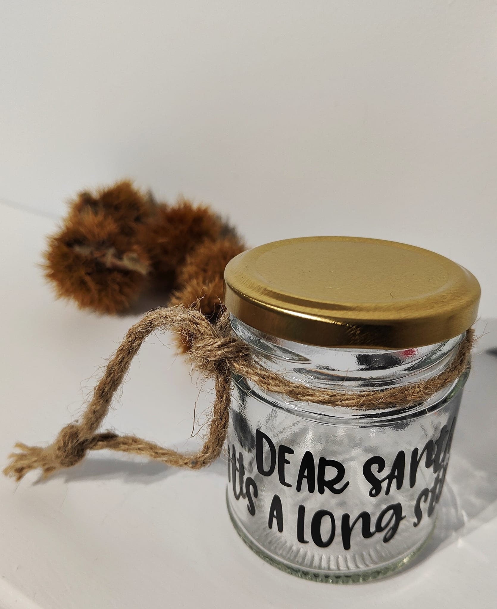 Glass jar with gold lid and natural jute, on a white background with chestnut husks scattered