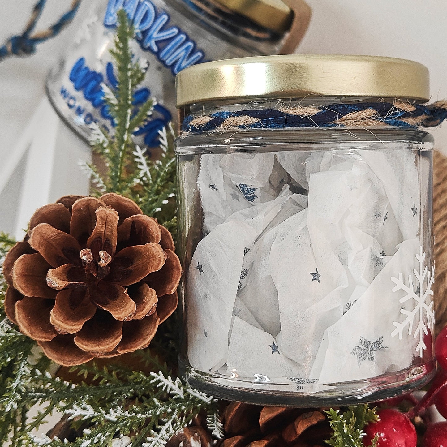 Glass jar showing the back of the jar with decorative items, pine cone, and Christmas decorations on a light background