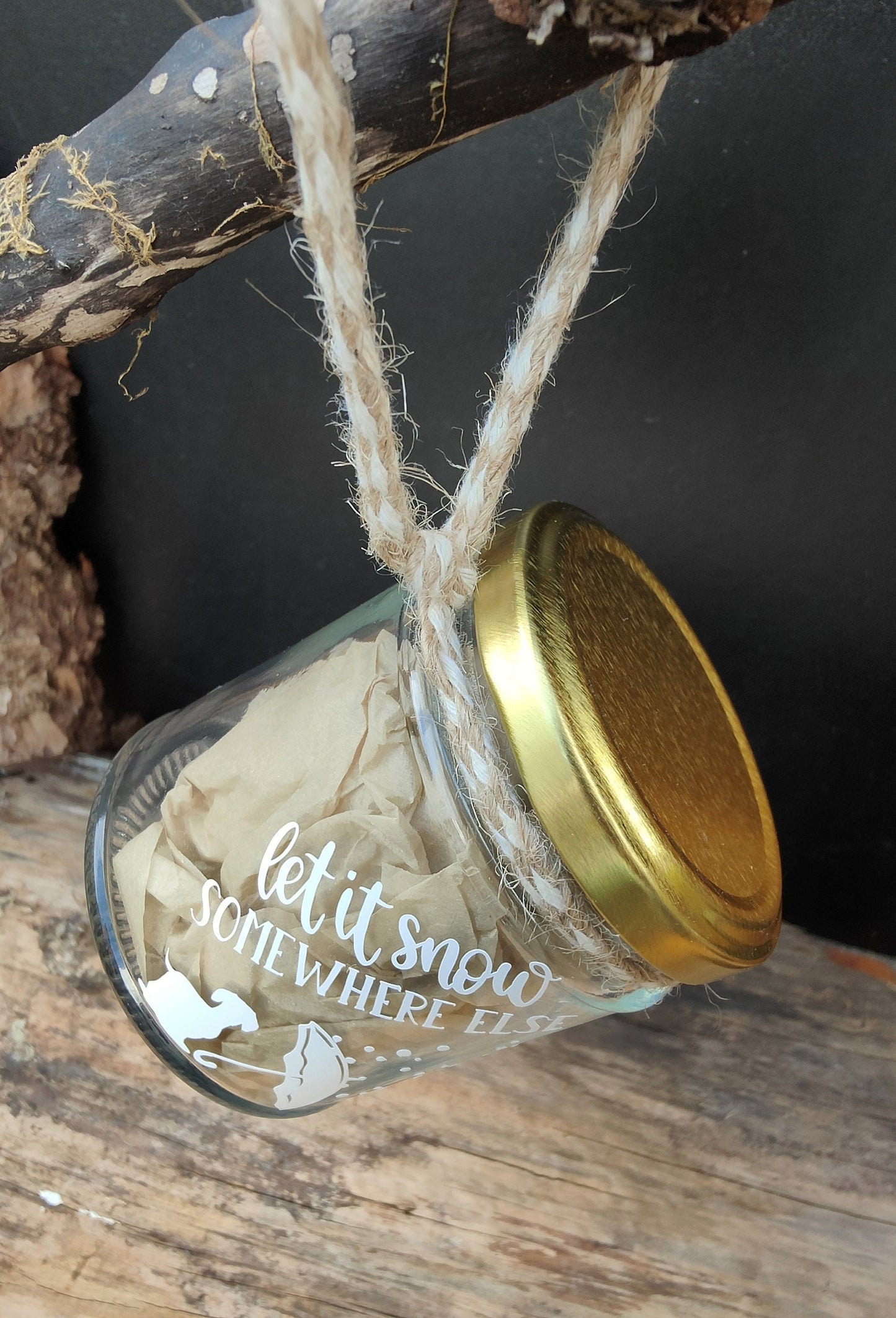 Dachshund-themed glass jar with gold lid and 'let it snow somewhere else' text, hanging on a branch with jute.