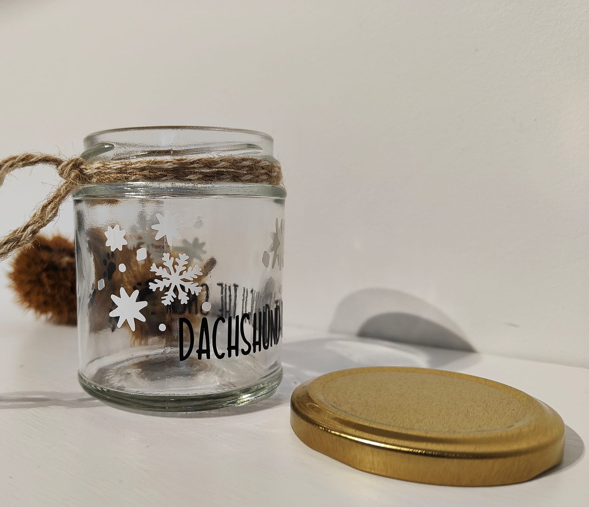 Glass jar with a gold lid against a white background. White Snowflakes and black text 'Dachshund Through The Snow...' are shown on the clear glass jar.