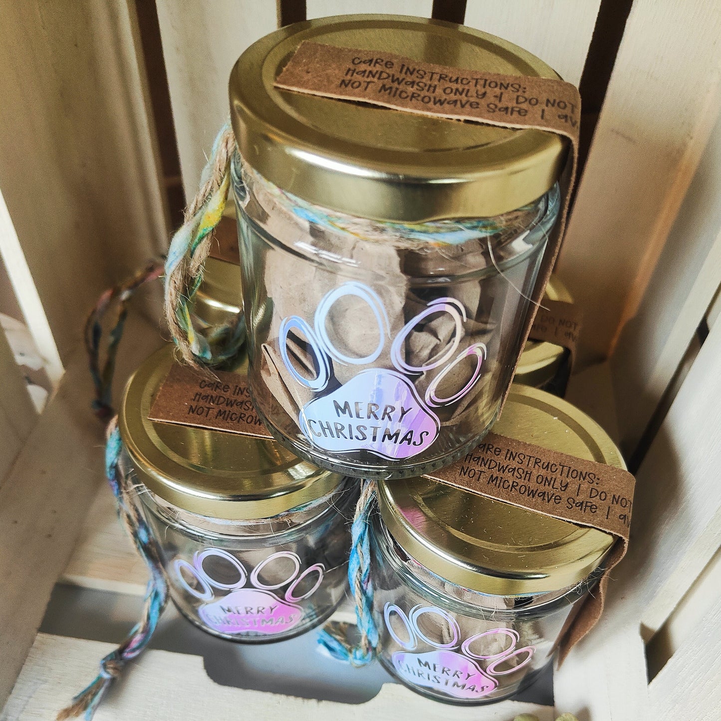 Three glass jars with gold lids and 'Merry Christmas' labels on a wooden surface.