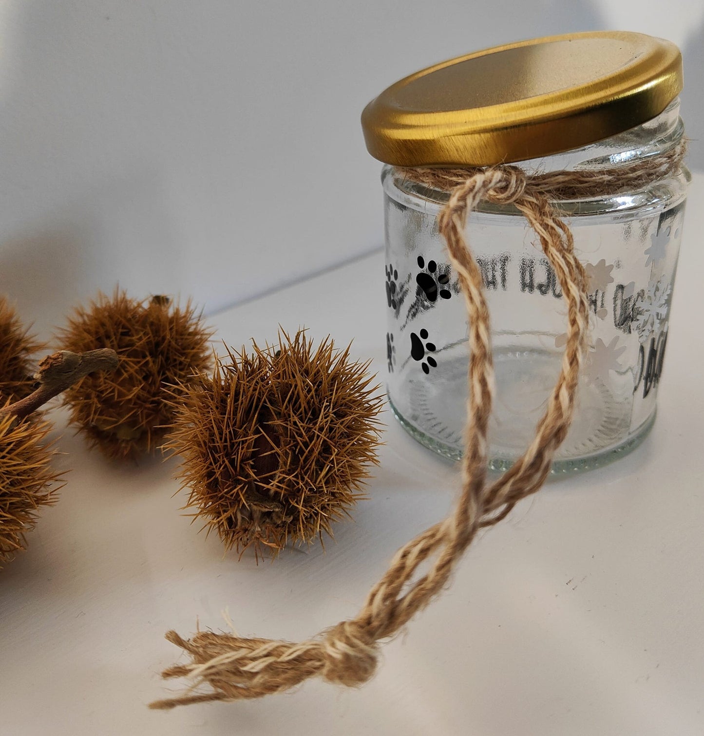 Glass jar with a gold lid and natural jute, surrounded by chestnuts on a white background