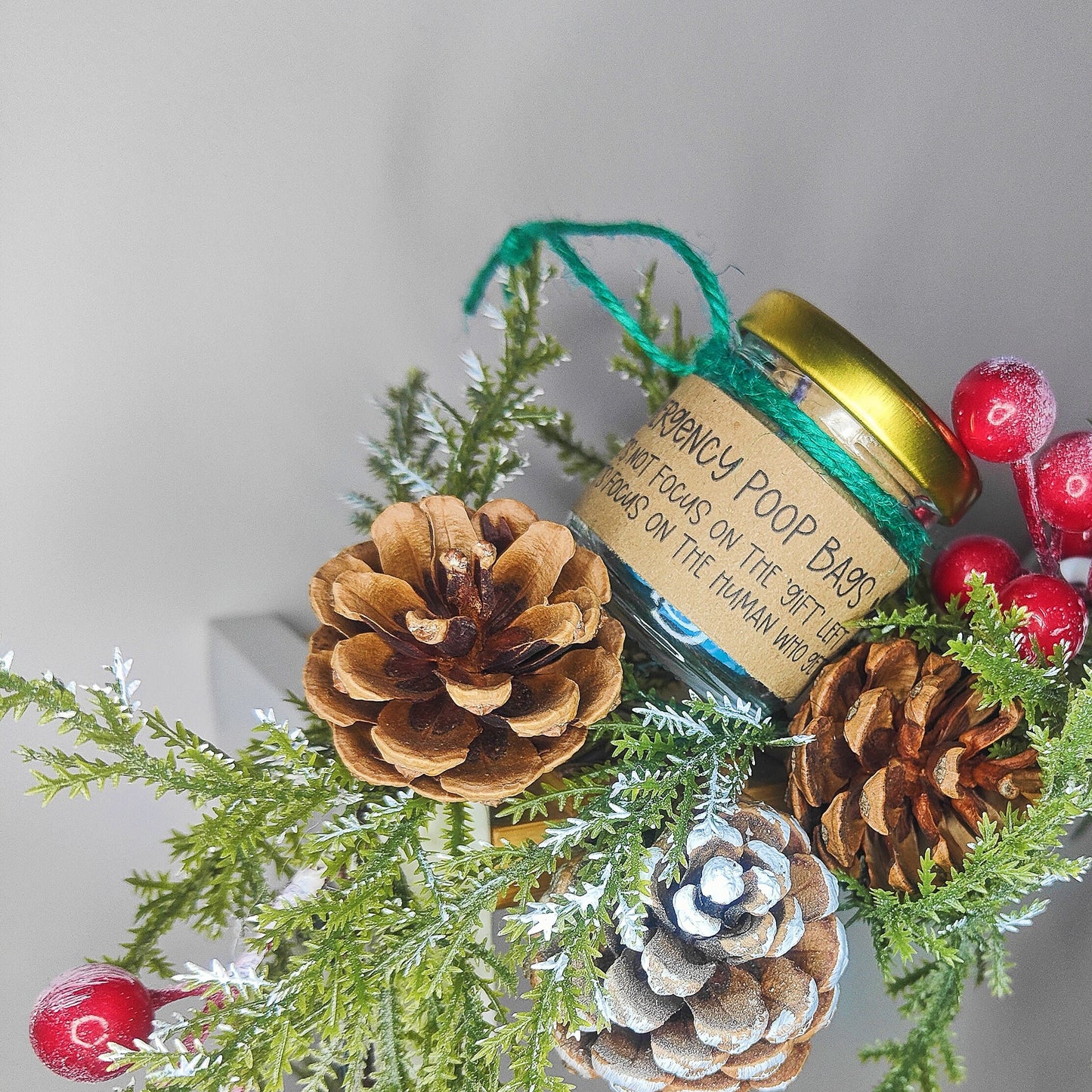 Small jar balanced between festive pine cones and berries.