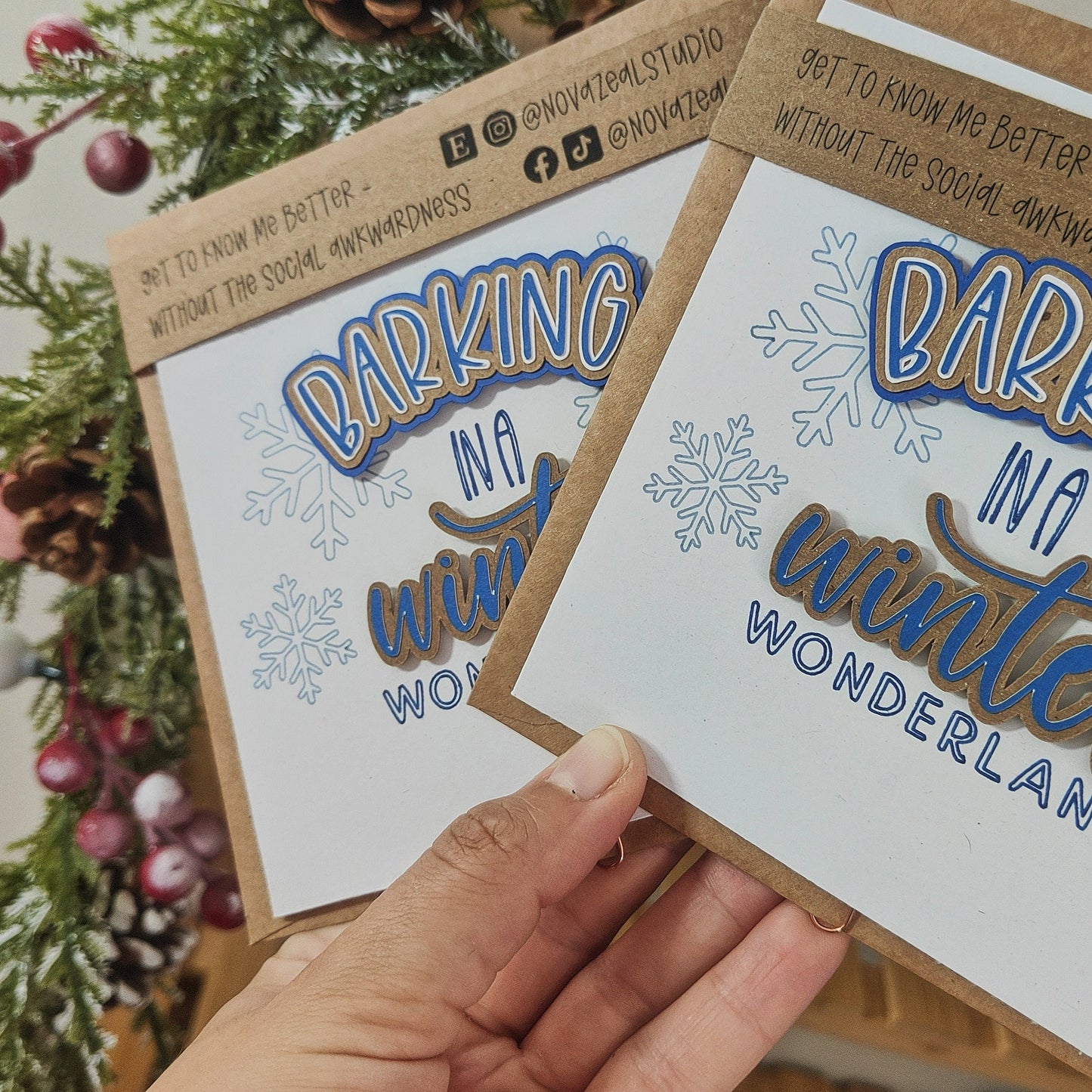 Two 'Barking in a Winter Wonderland' greeting cards held by a hand with a Christmas tree in the background.