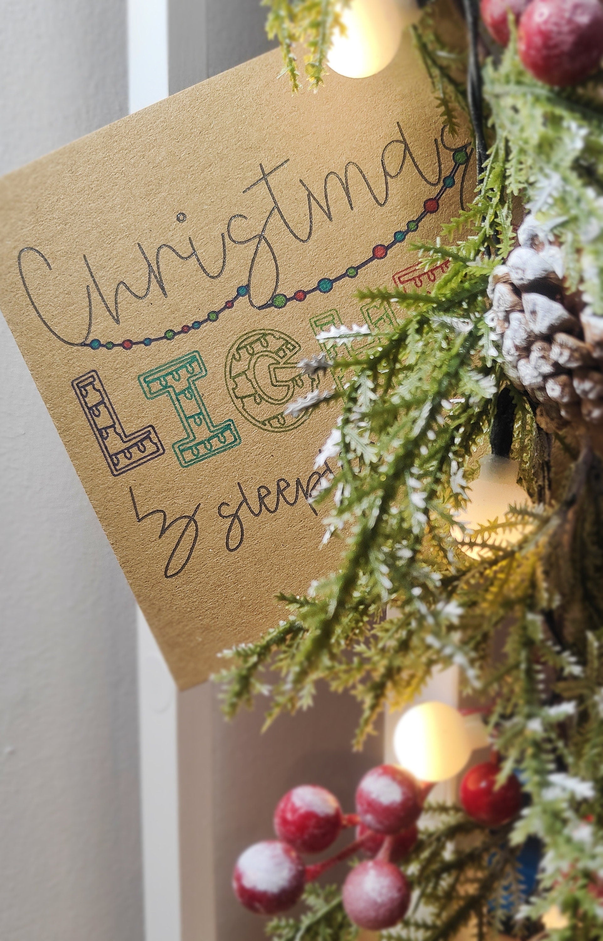 Christmas Card behind decorative  lights, greenery and berries on a white background