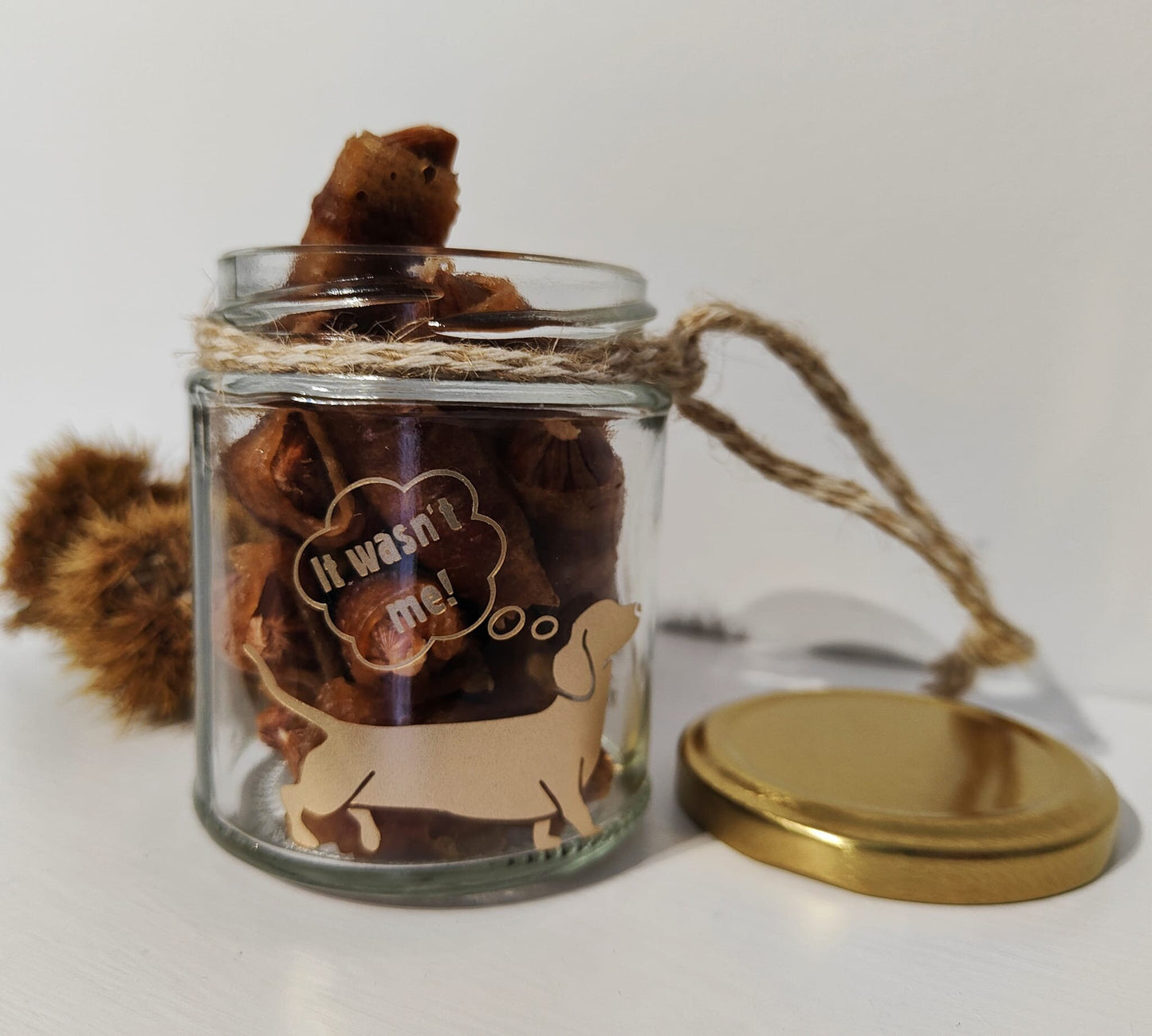 Glass jar with a gold lid containing treats, tied with natural jute on a white background.