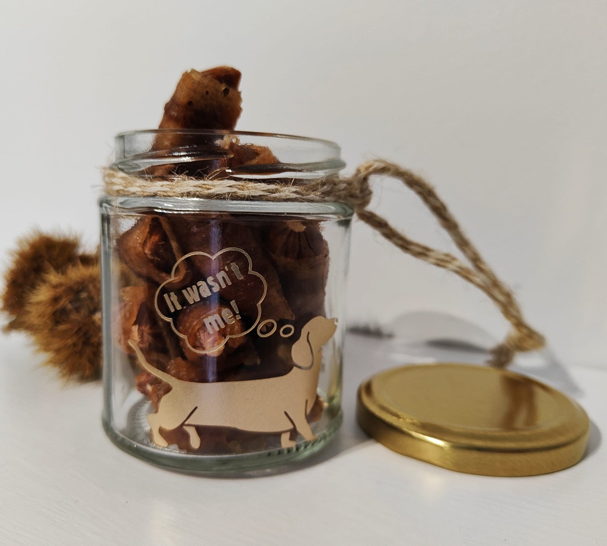 Glass jar with a gold lid containing treats, tied with natural jute on a white background.