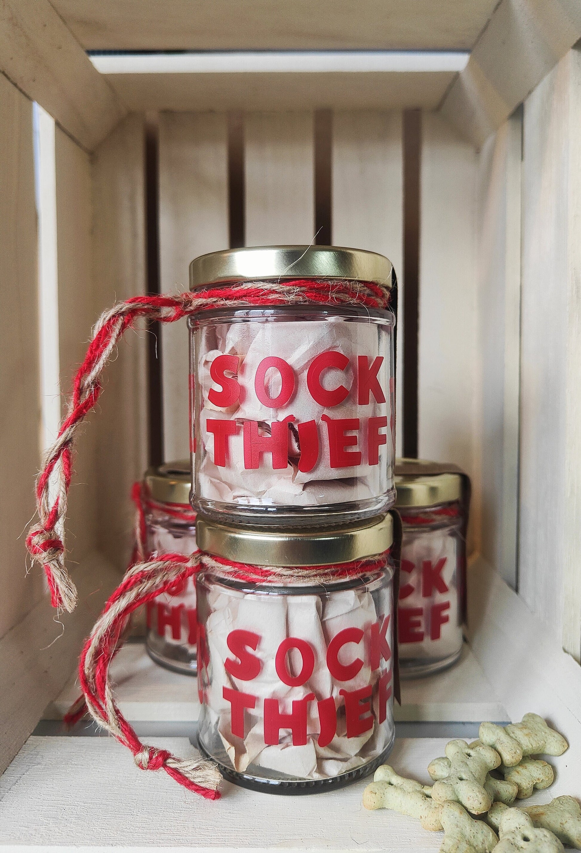 Empty Jars labeled 'Sock Thief', tied with red and natural jute for hanging, in a wooden crate.