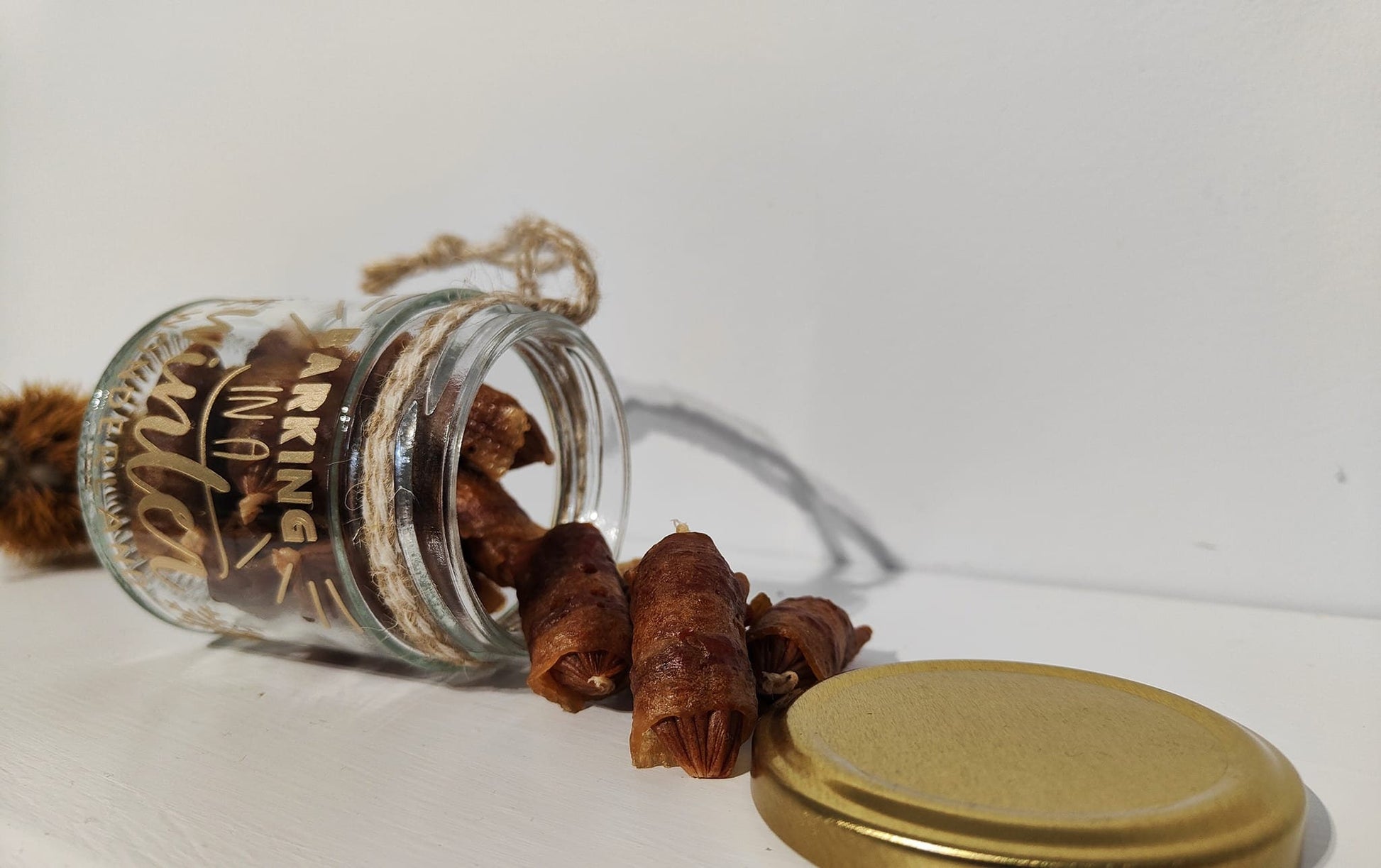 Glass jar lying on its side with gold lid and treats spilling out on a white background