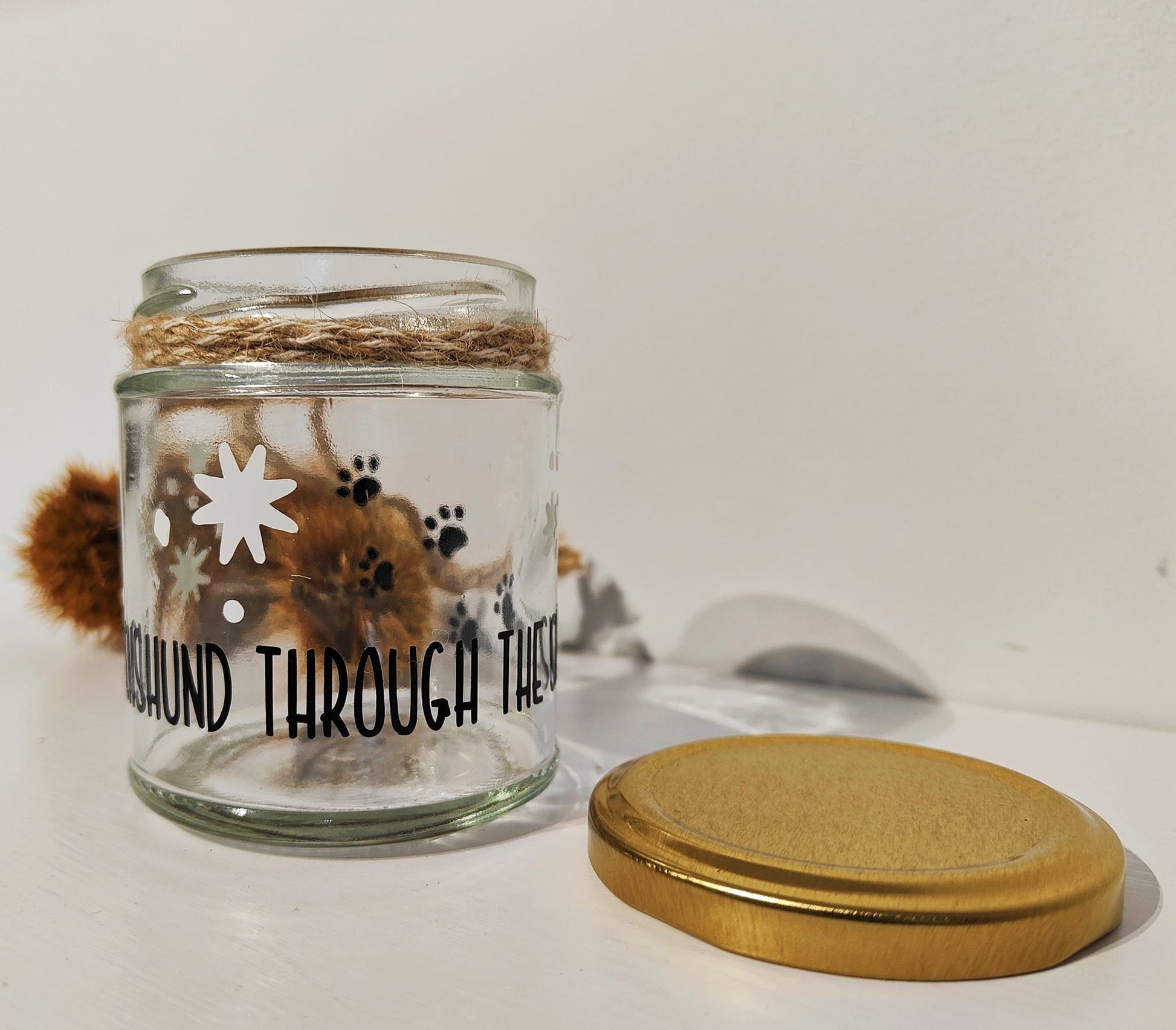 Glass jar with natural jute shown around the neck of the jar, dog-themed Christmas treat jar, placed on a white surface.