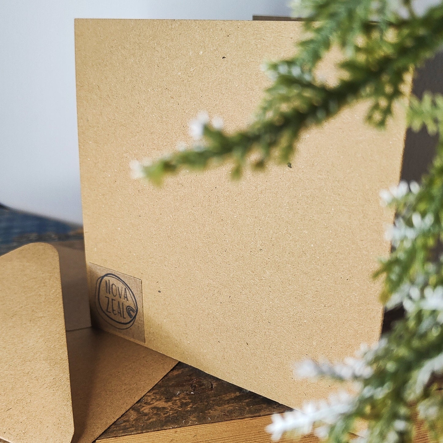 Close-up of the back of the Christmas card with a visible brand logo 'Nova Zeal', featuring greenery in the background.