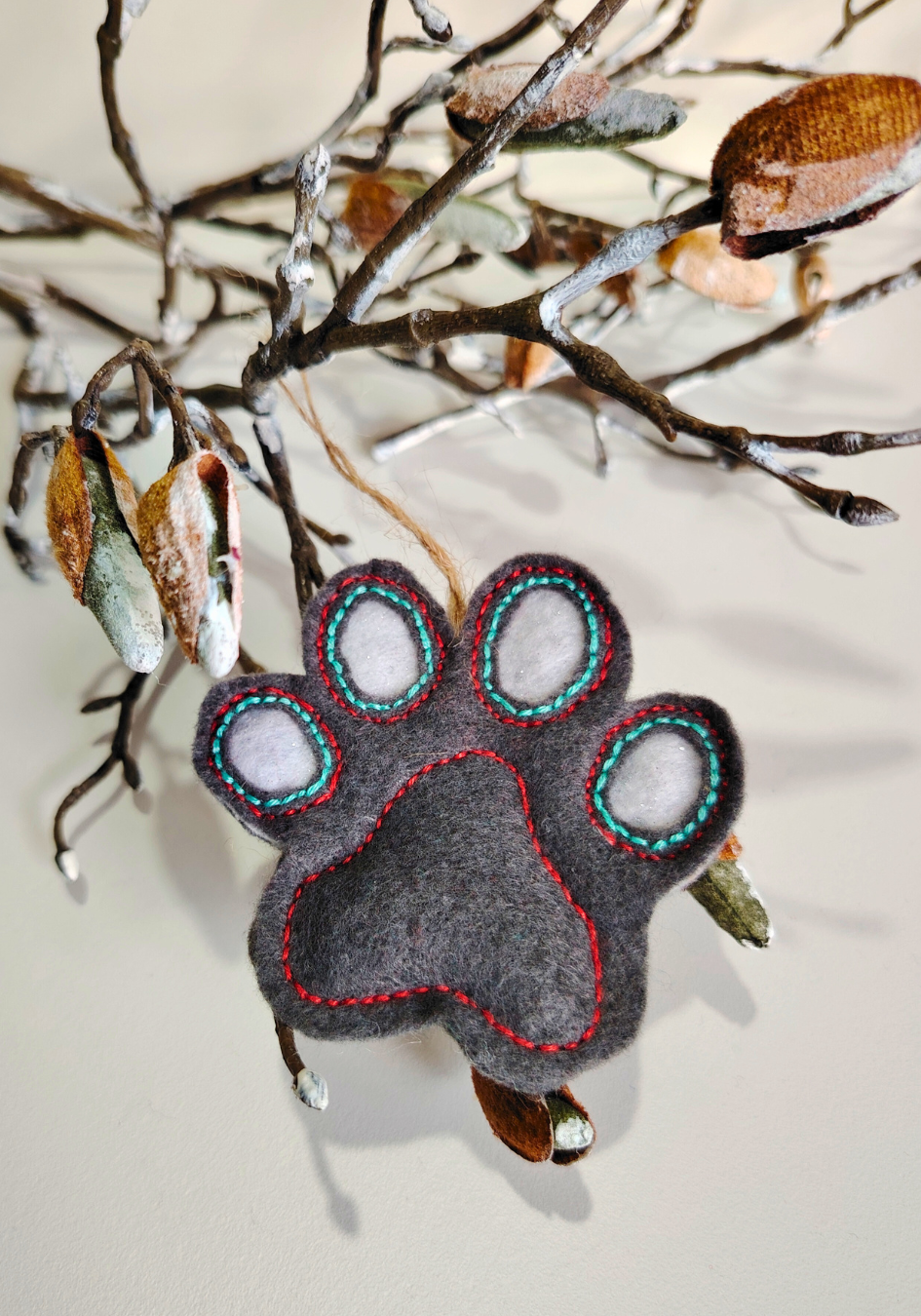 Felt paw print ornament hanging on a branch with a snowy white background