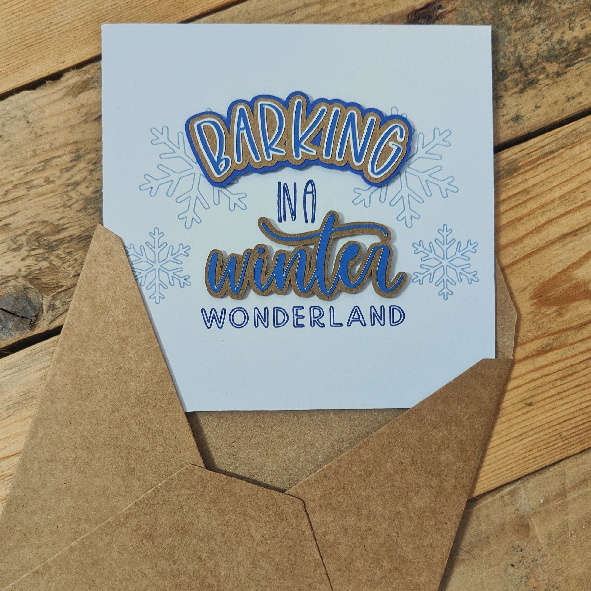 White Christmas card with 'Barking in a winter wonderland' text on a wooden surface.