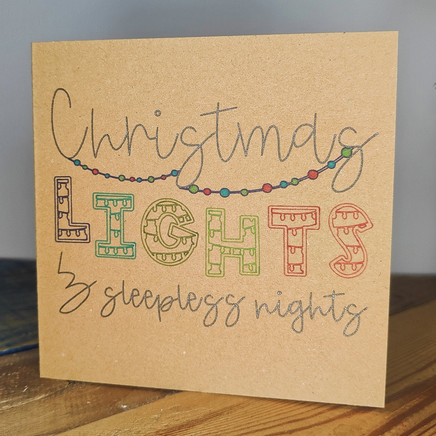 Handmade card with 'Christmas Lights & Sleepless Nights' text and string of lights design on kraft card.