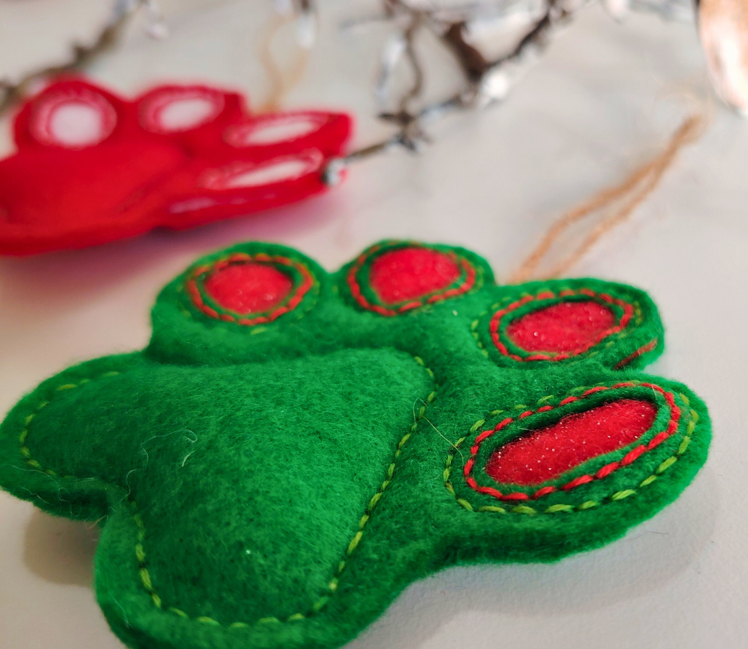 Green felt paw print with red accents on a light background showing the handstitched details 