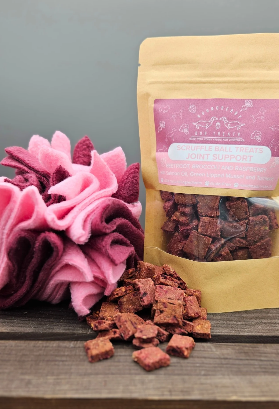 Bag of dog treats with pink packaging and matching snuffle ball  on a wooden surface