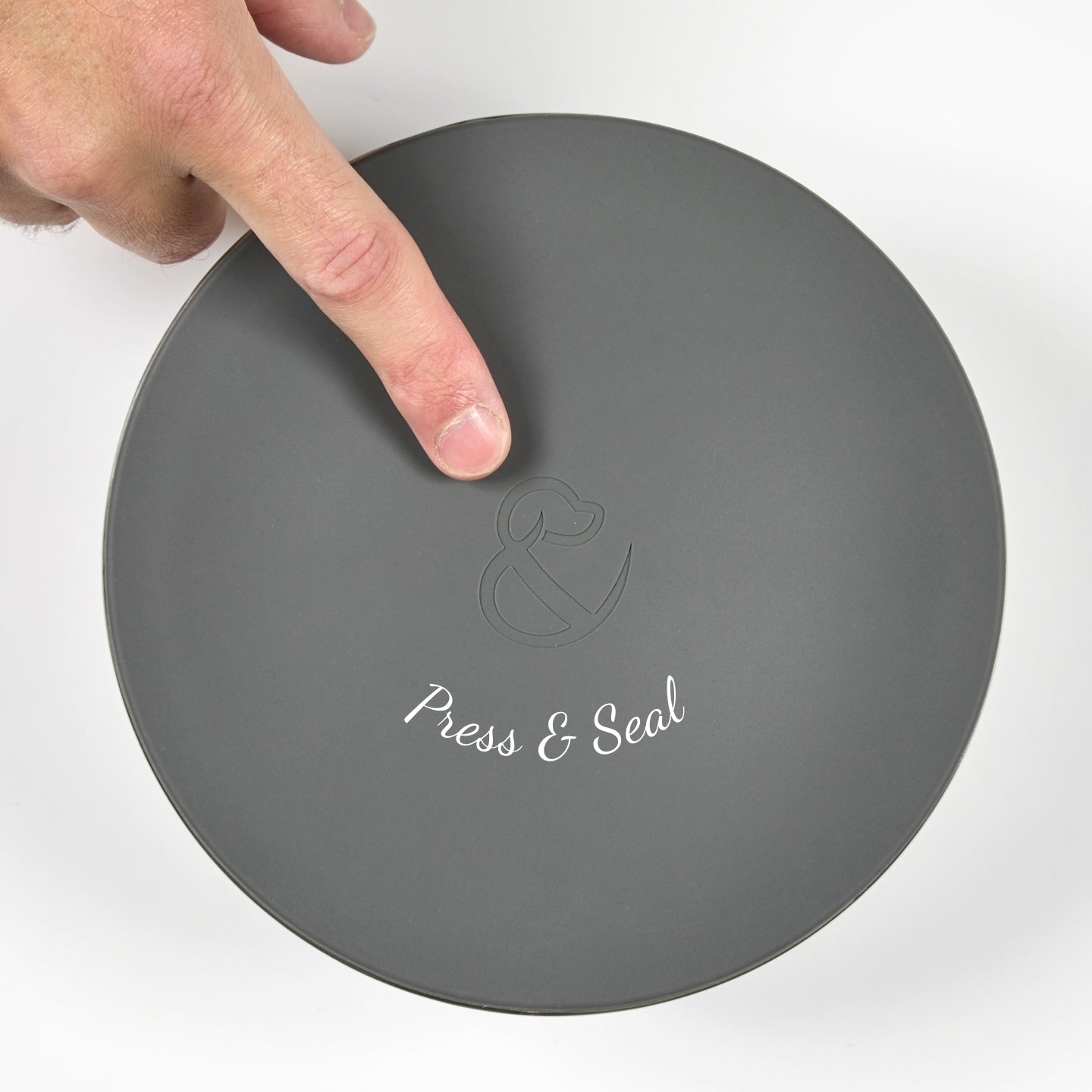 Top-down view of a hand pressing down on the Pup & Kit Lid-it bowl lid, demonstrating the airtight push and seal feature.