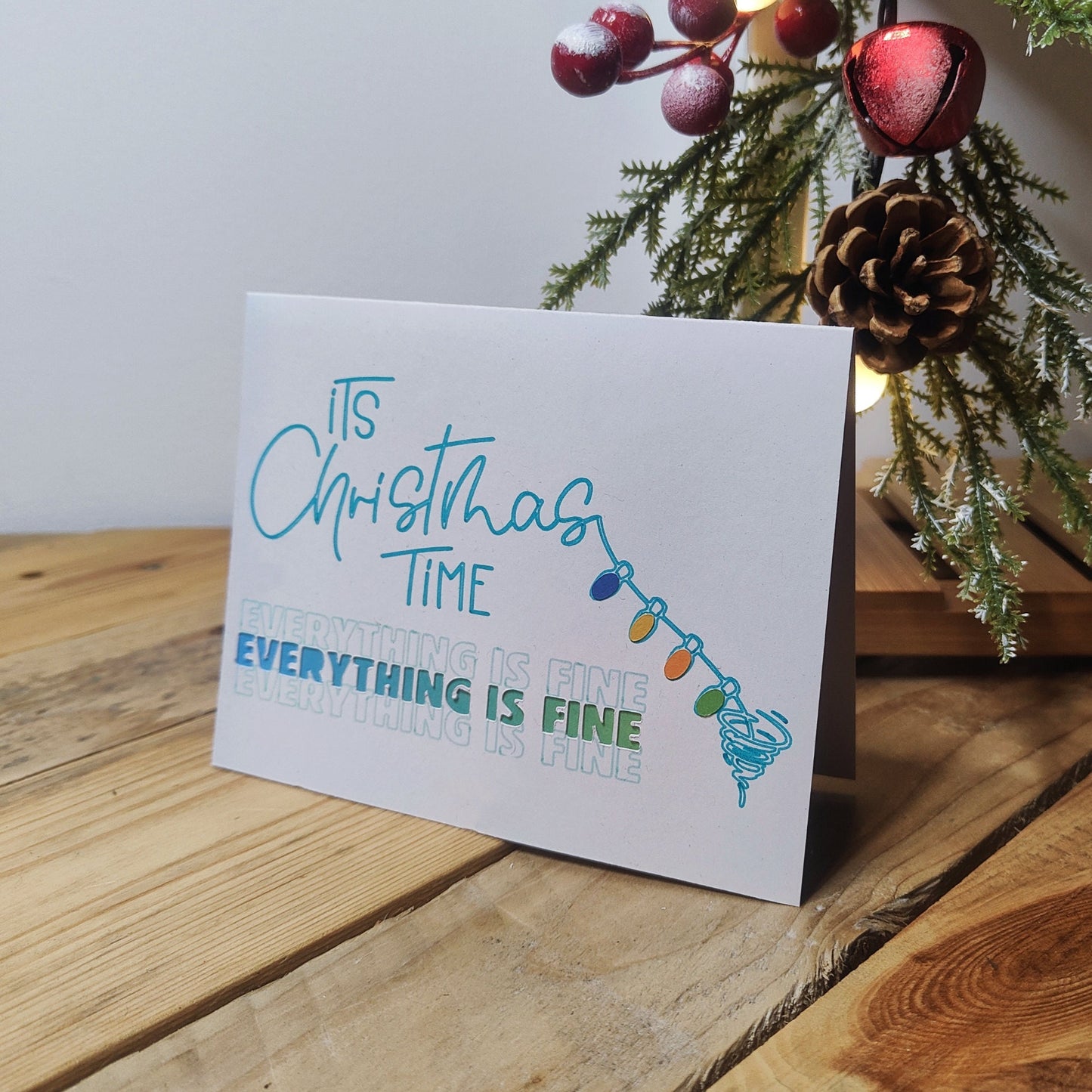 Dog Owner Christmas card with festive text and lights on a wooden surface with a Christmas tree in the background.