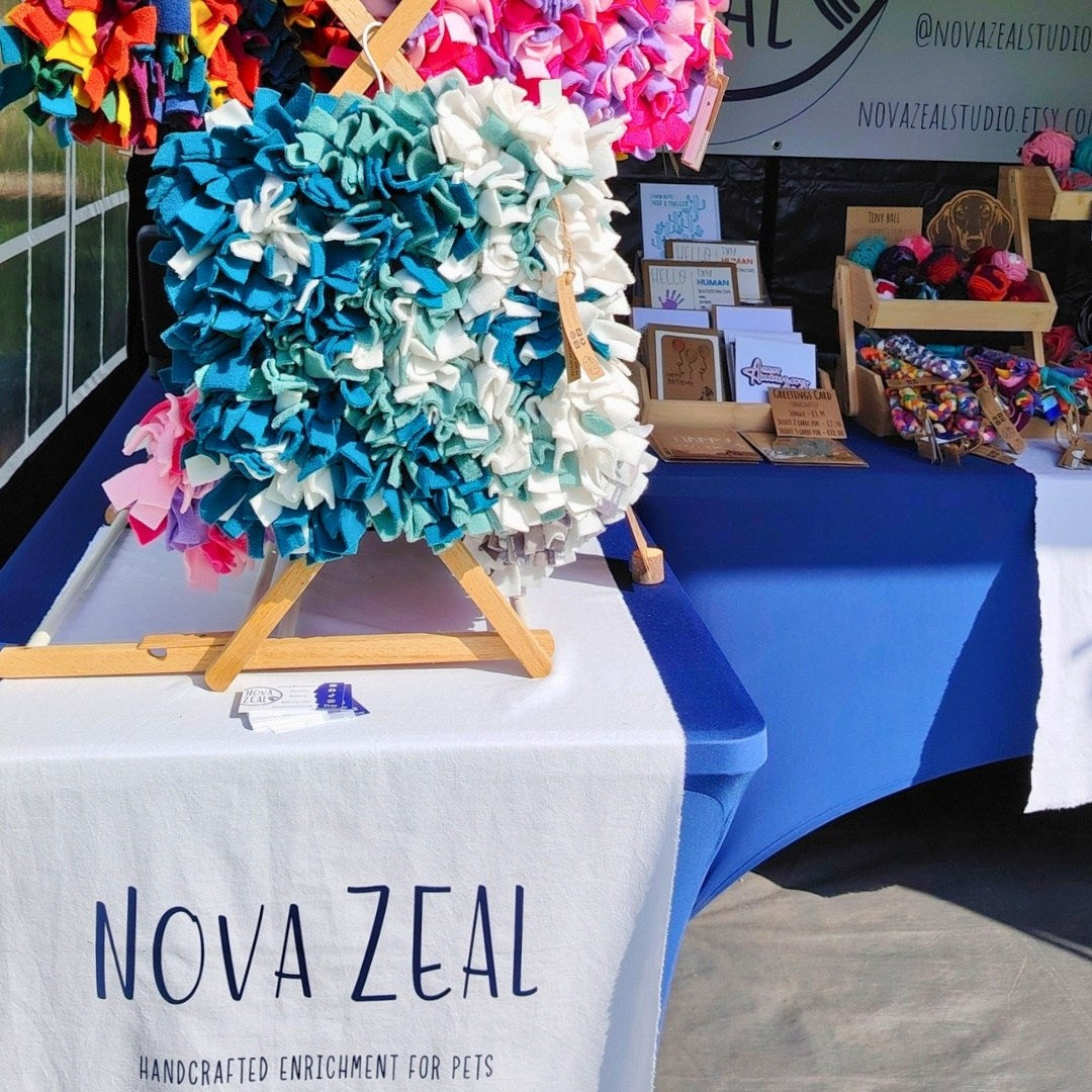 Colorful handmade items on display at a Nova Zeal stand with a blue tablecloth.
