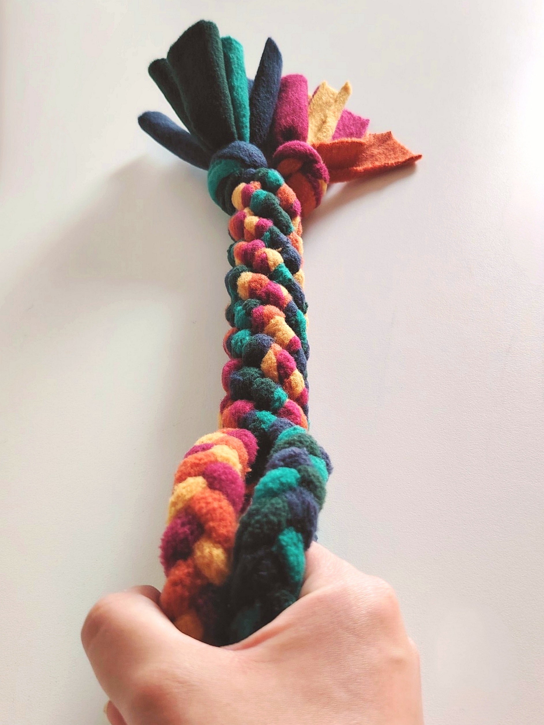 Hand holding warm colour fleece dog tug toy showing interactive play use.
