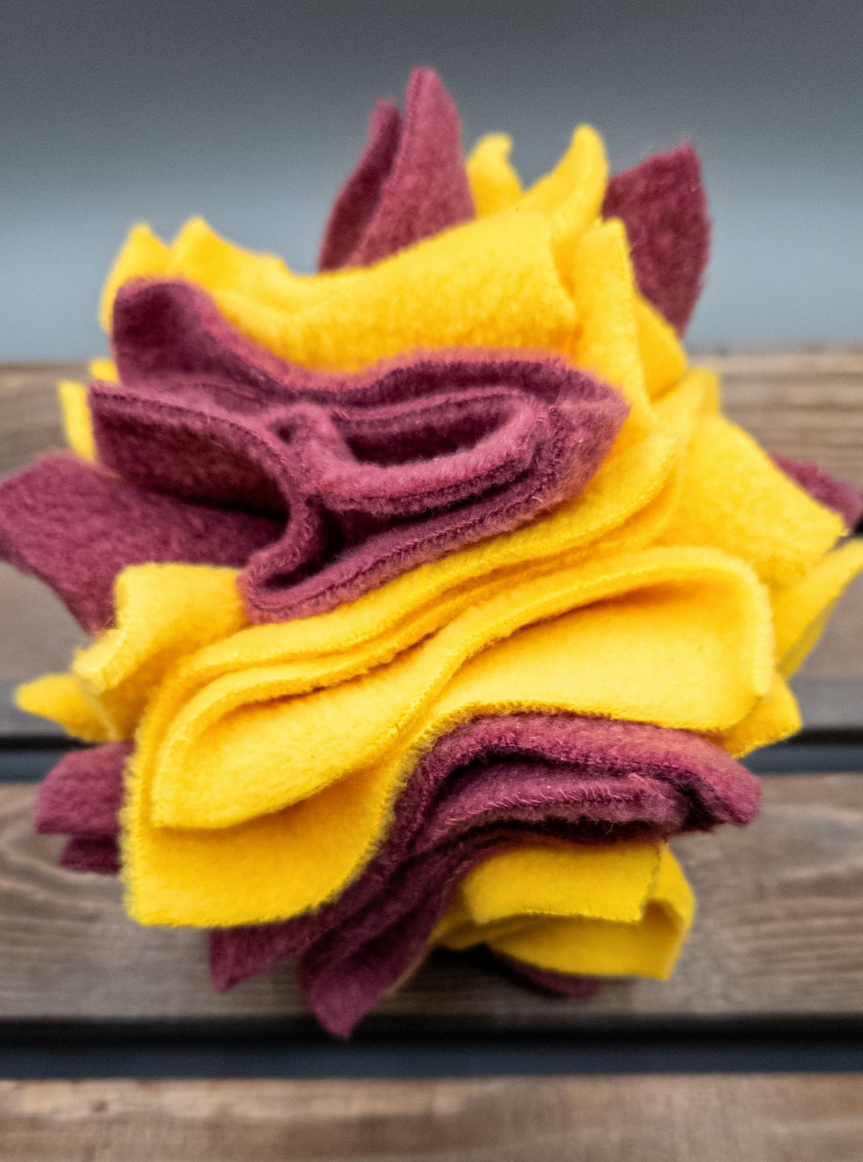 Yellow and maroon fleece interactive toy on a wooden surface with a grey background