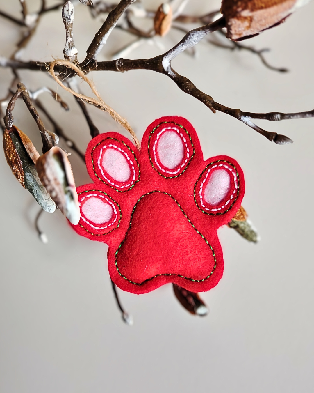 Red paw print ornament hanging on a branch with a neutral background