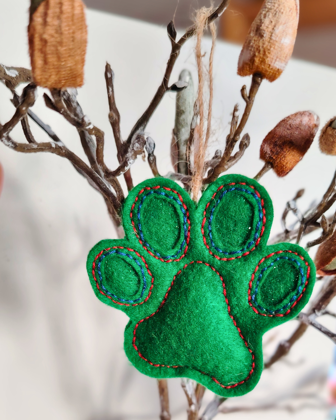 Green paw-shaped ornament hanging on a branch with dried leaves.