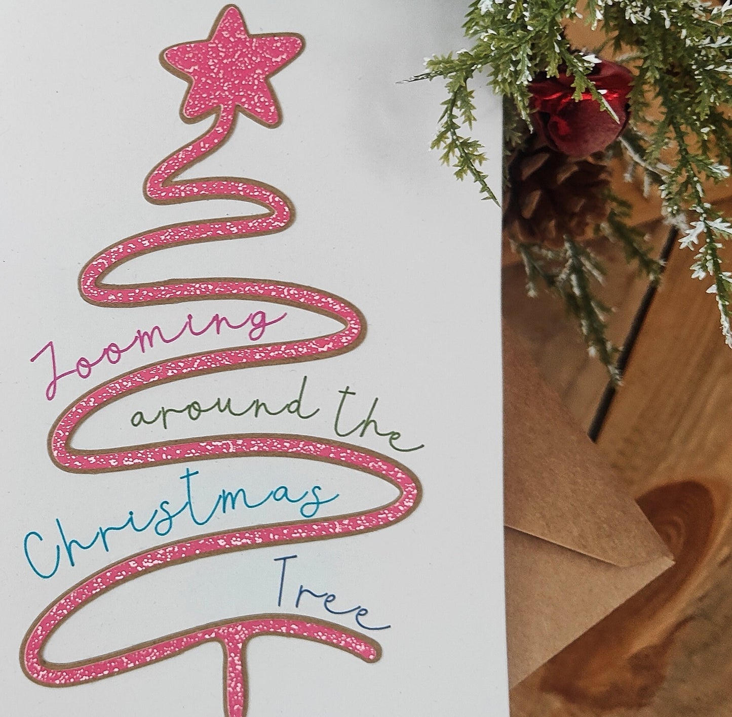 Pink glittery Christmas tree design with text on a white background, next to a Christmas tree branch.