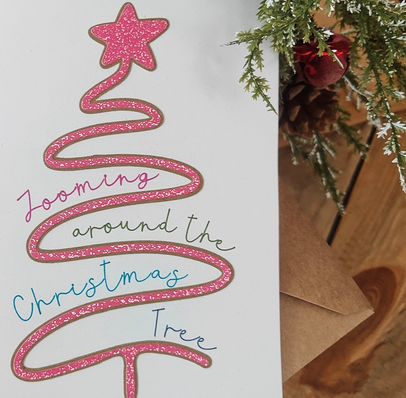 Pink glittery Christmas tree design with text on a white background, next to a Christmas tree branch.
