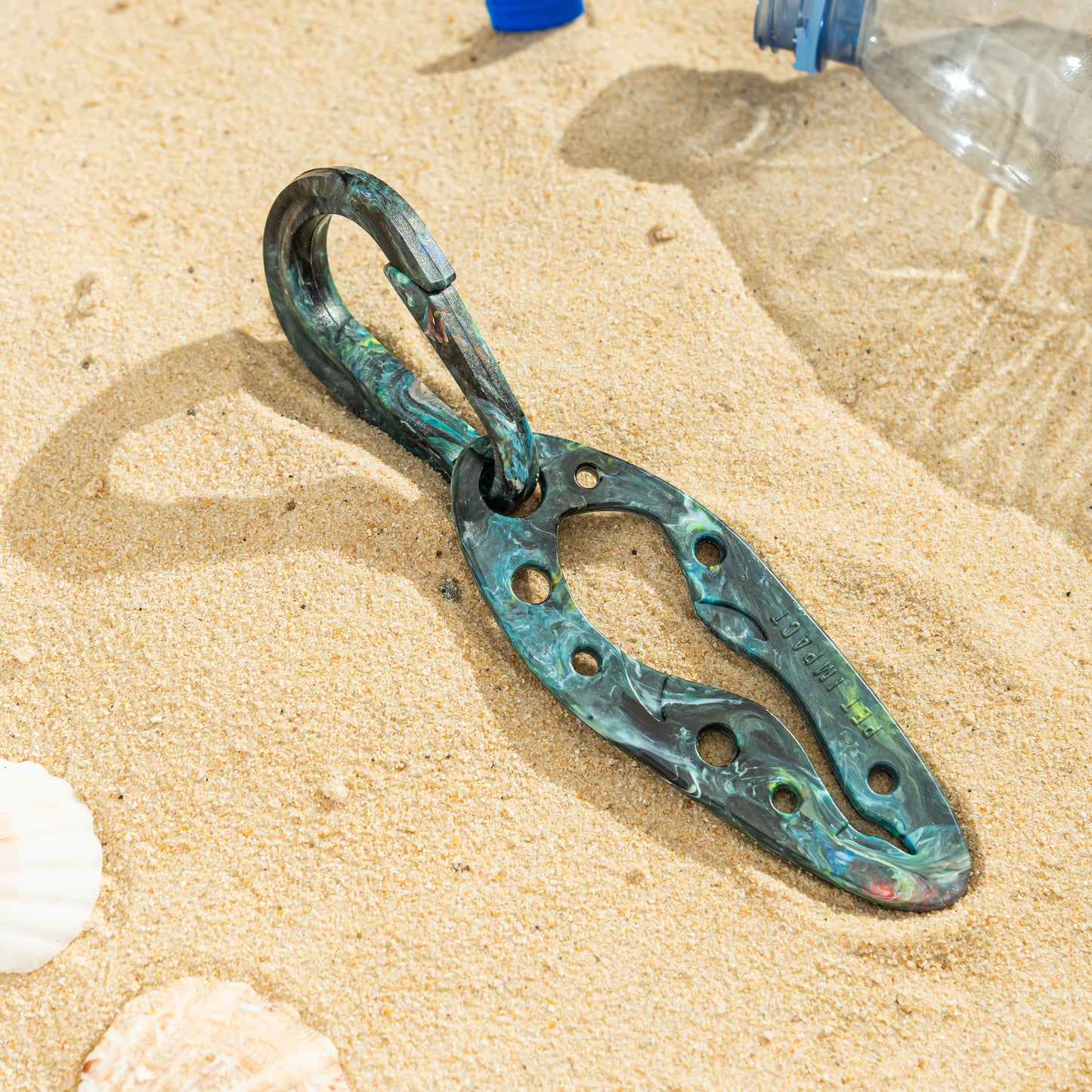 Nebula PooPal in a blue, green and black marbled finish with matching carabiner, photographed on a sandy surface.