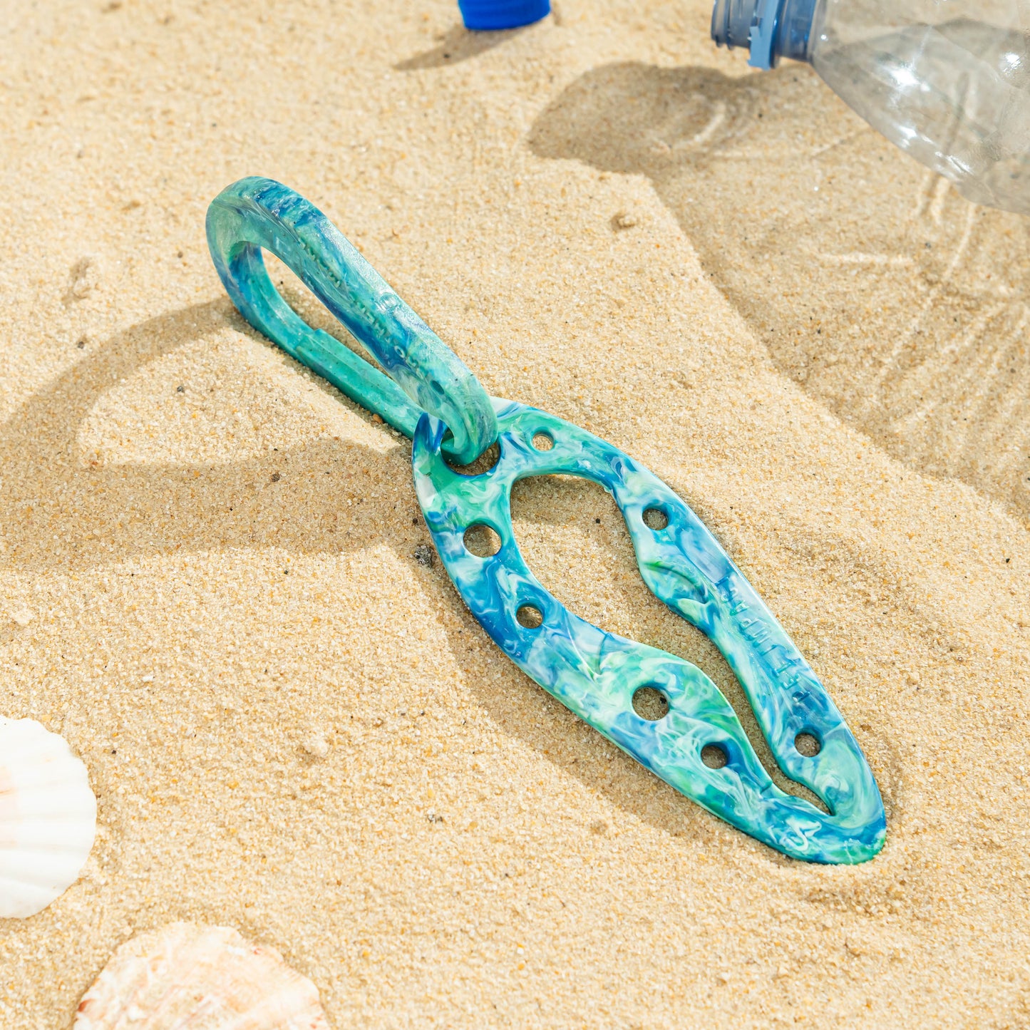 Tropical Whirlpool PooPal in a turquoise, white and green marbled finish with matching carabiner, photographed on a sandy surface.
