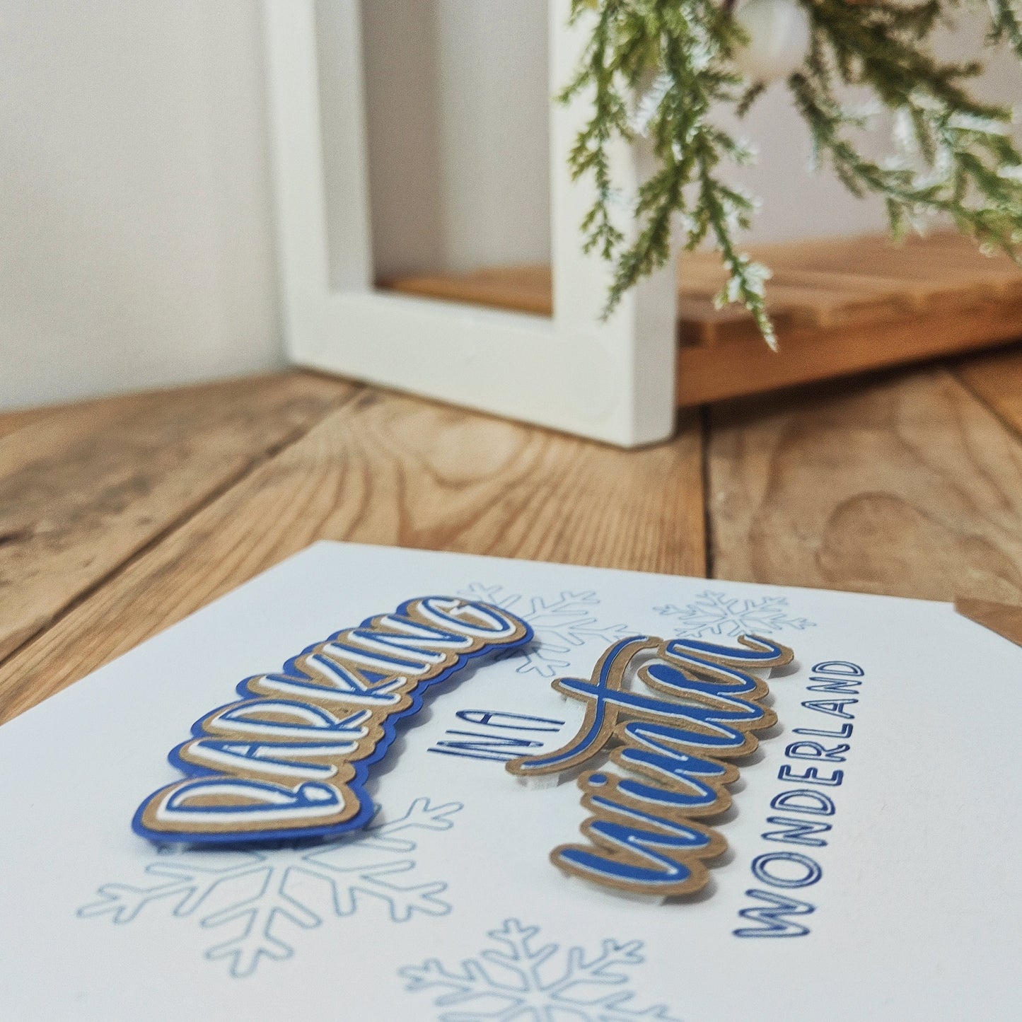 Greetings card showing the raised text, 'Barking in a Winter Wonderland', on a wooden surface with Christmas decor in the background.