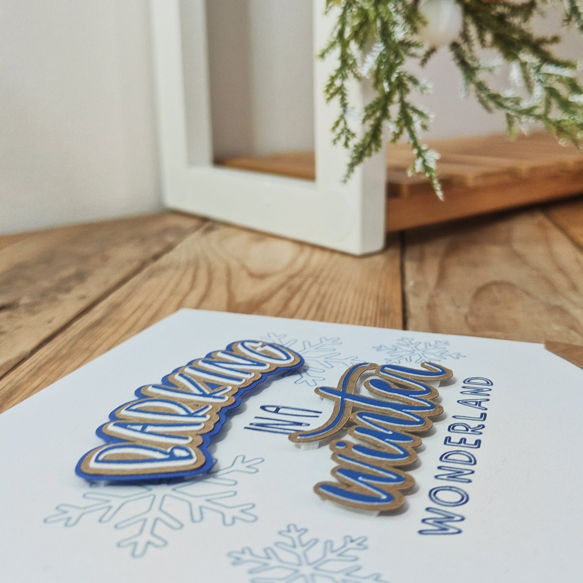 Greetings card showing the raised text, 'Barking in a Winter Wonderland', on a wooden surface with Christmas decor in the background.