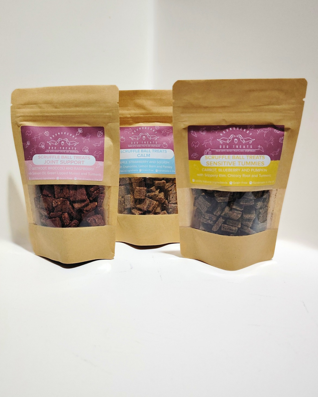 Three kraft treat bags with transparent windows displaying the three varieties of dried treats on a white background