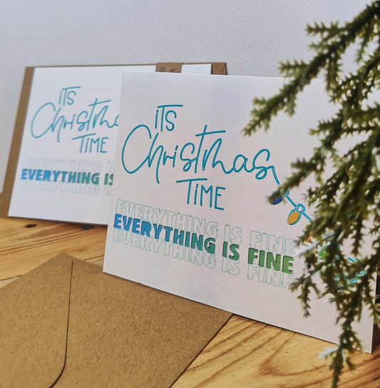 Two Christmas-themed greeting cards on a wooden surface with a branch in the background.