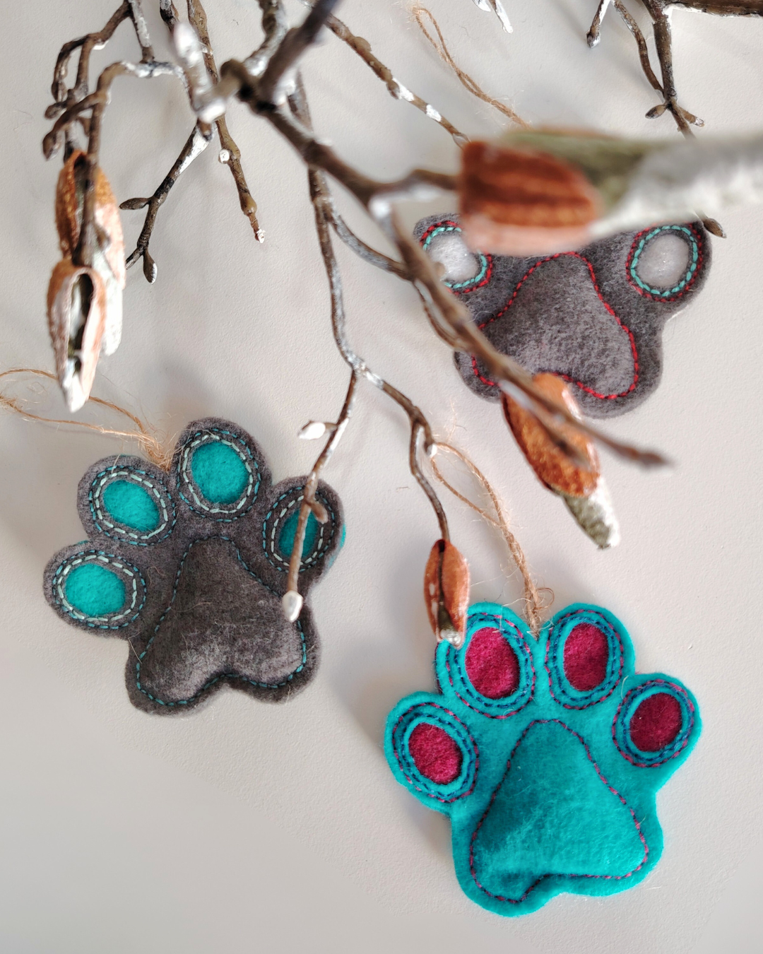 Three grey and turquoise felt paw print decorations under a branch 