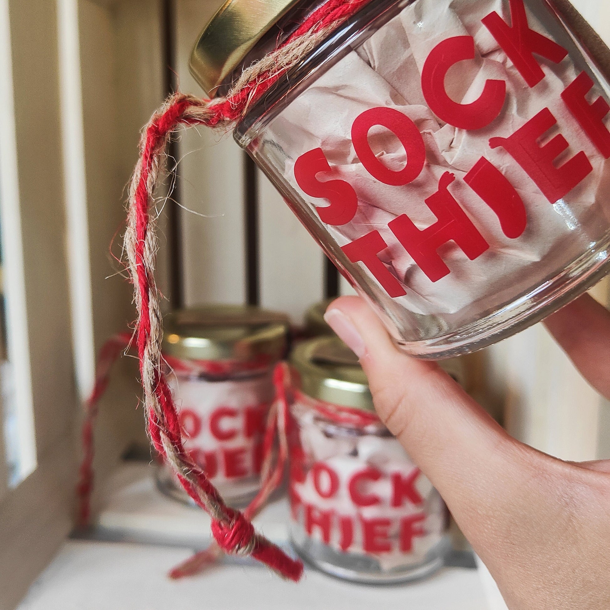 Glass jar labeled 'Sock Thief' with red text, held by a hand with more jars in the background.