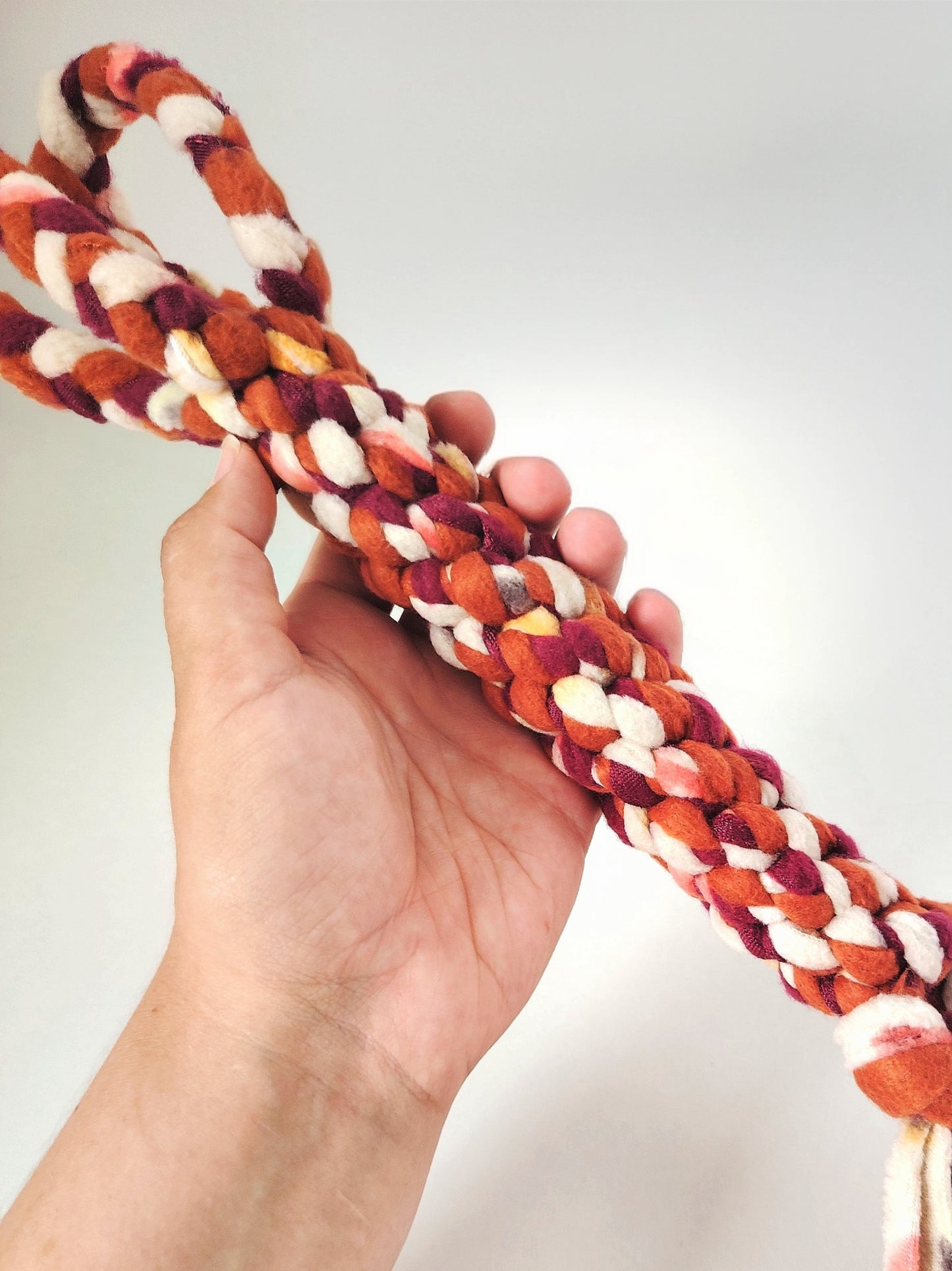 Hand holding an Autumn handled dog tug toy made from braided fleece in warm seasonal colours.