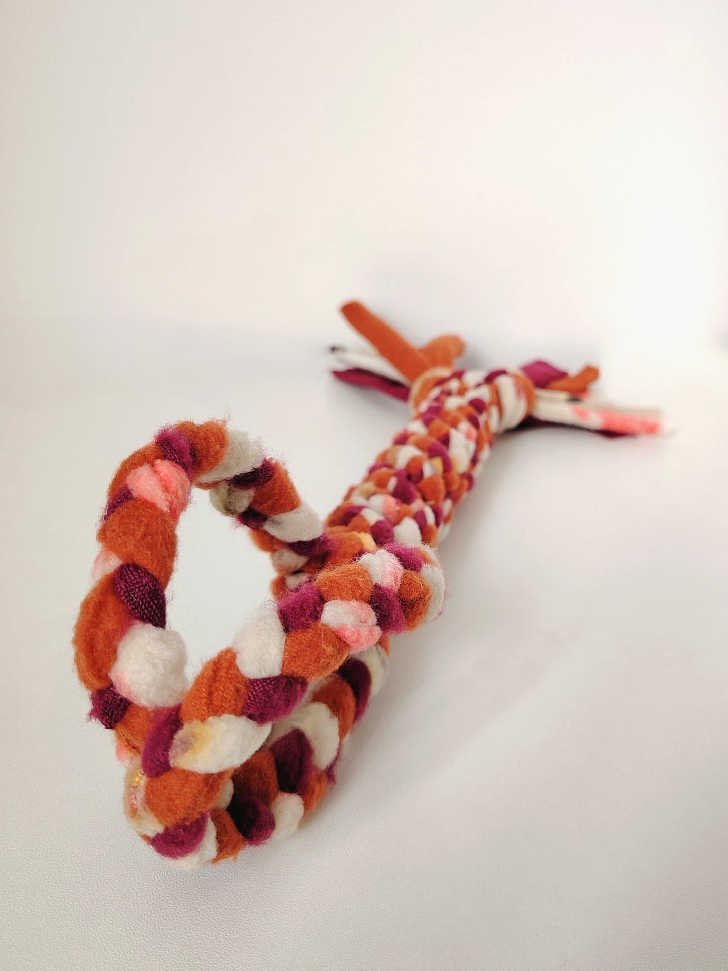 Autumn handled dog tug toy laid out to show the braided fleece handle, body and tasselled end.